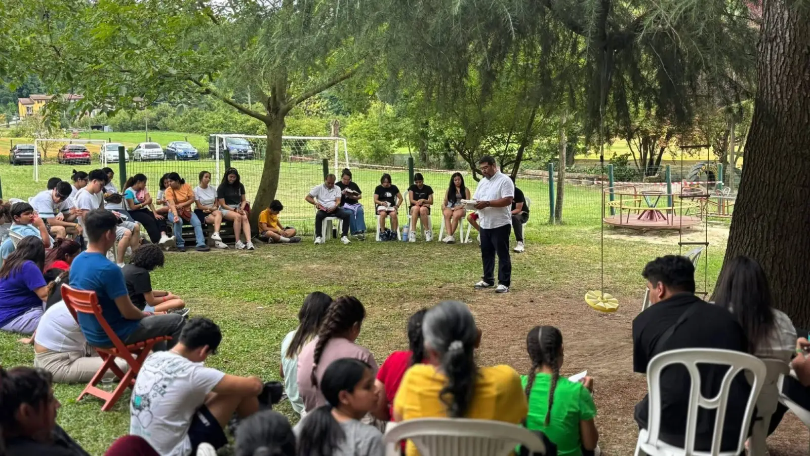 Giovani e famiglie seduti in cerchio all’aperto durante un momento di lettura della Bibbia