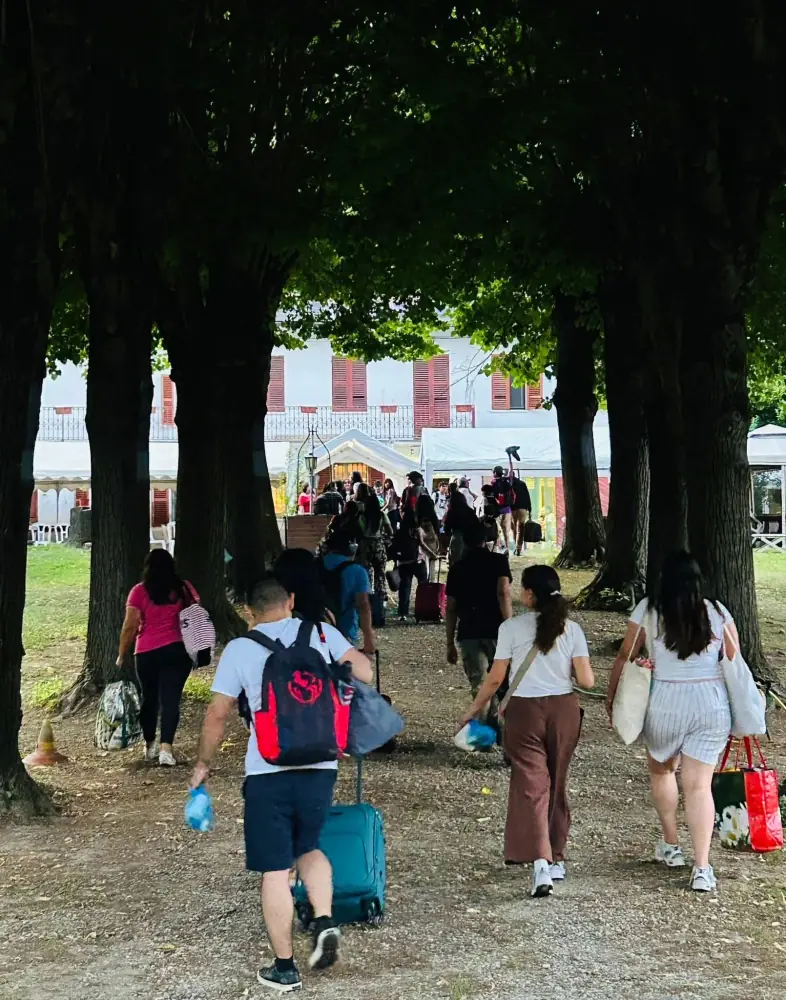 Un gruppo di persone con valigie e borse cammina lungo un viale alberato
